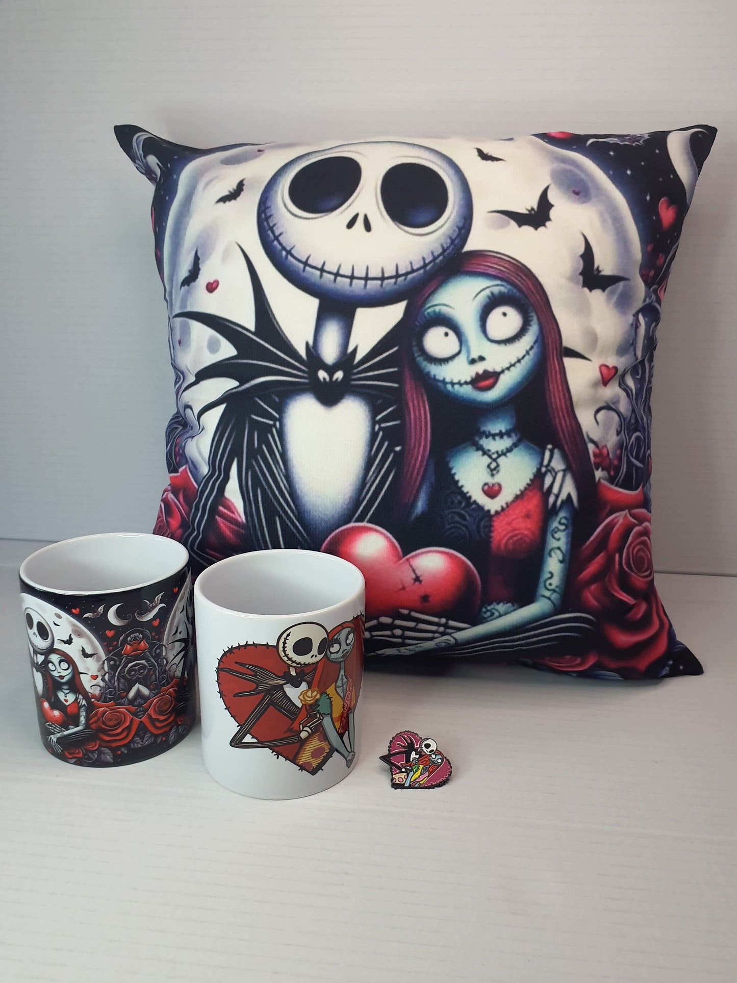 Detalle del cojín con ilustración de personajes oscuros estilo retro sobre fondo de la luna, más dos tazas y un pin a juego.