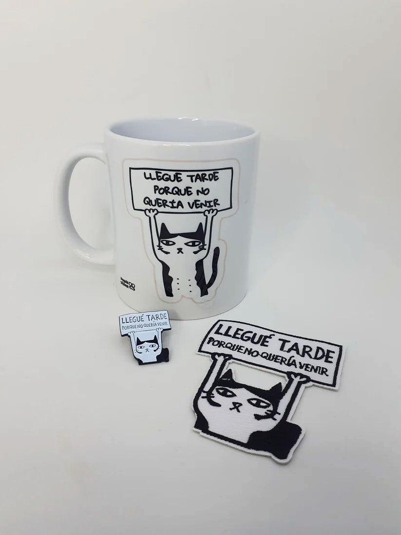 "Pack de taza, pin y parche con diseño de gato sosteniendo un cartel que dice 'Llegué tarde porque no quería venir'."