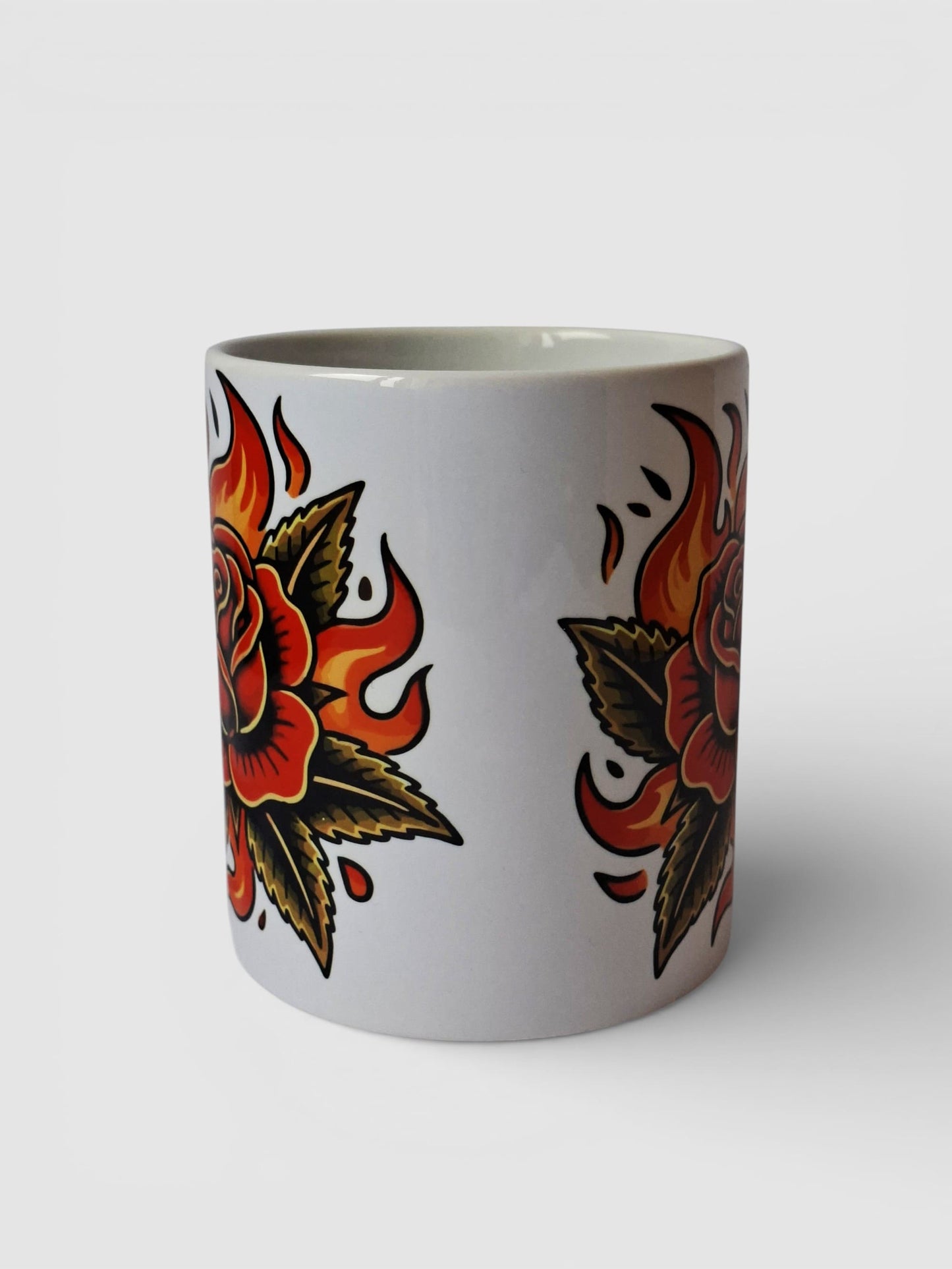 "Taza de cerámica con rosa en llamas old school, diseño de tatuaje tradicional ideal para amantes del arte retro."