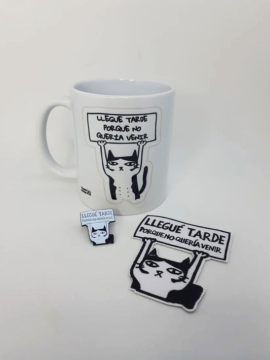 "Pack de taza, pin y parche con diseño de gato sosteniendo un cartel que dice 'Llegué tarde porque no quería venir'."