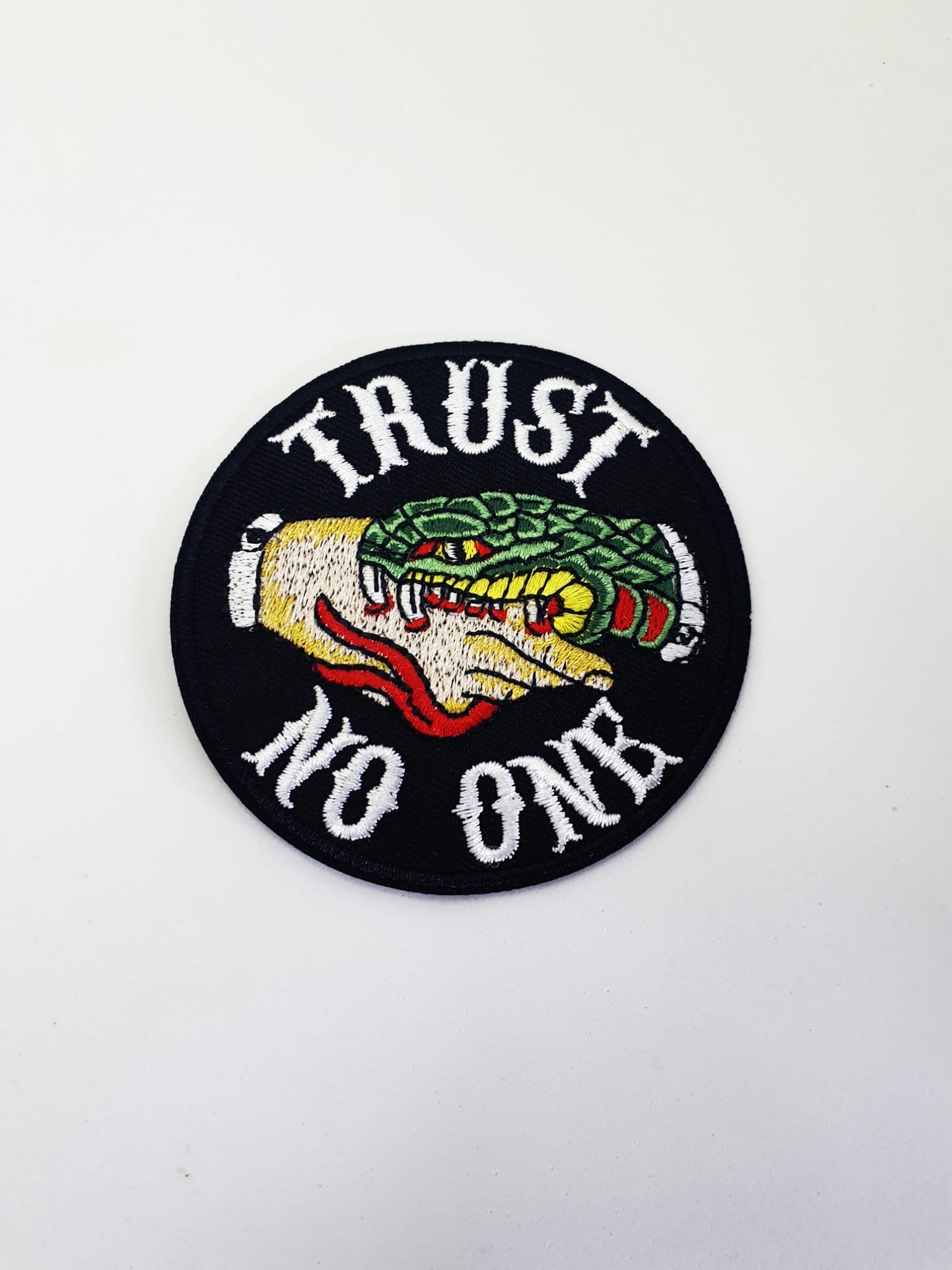 Parche bordado circular con mensaje rebelde Trust No One y motivos inspirados en tatuaje tradicional.