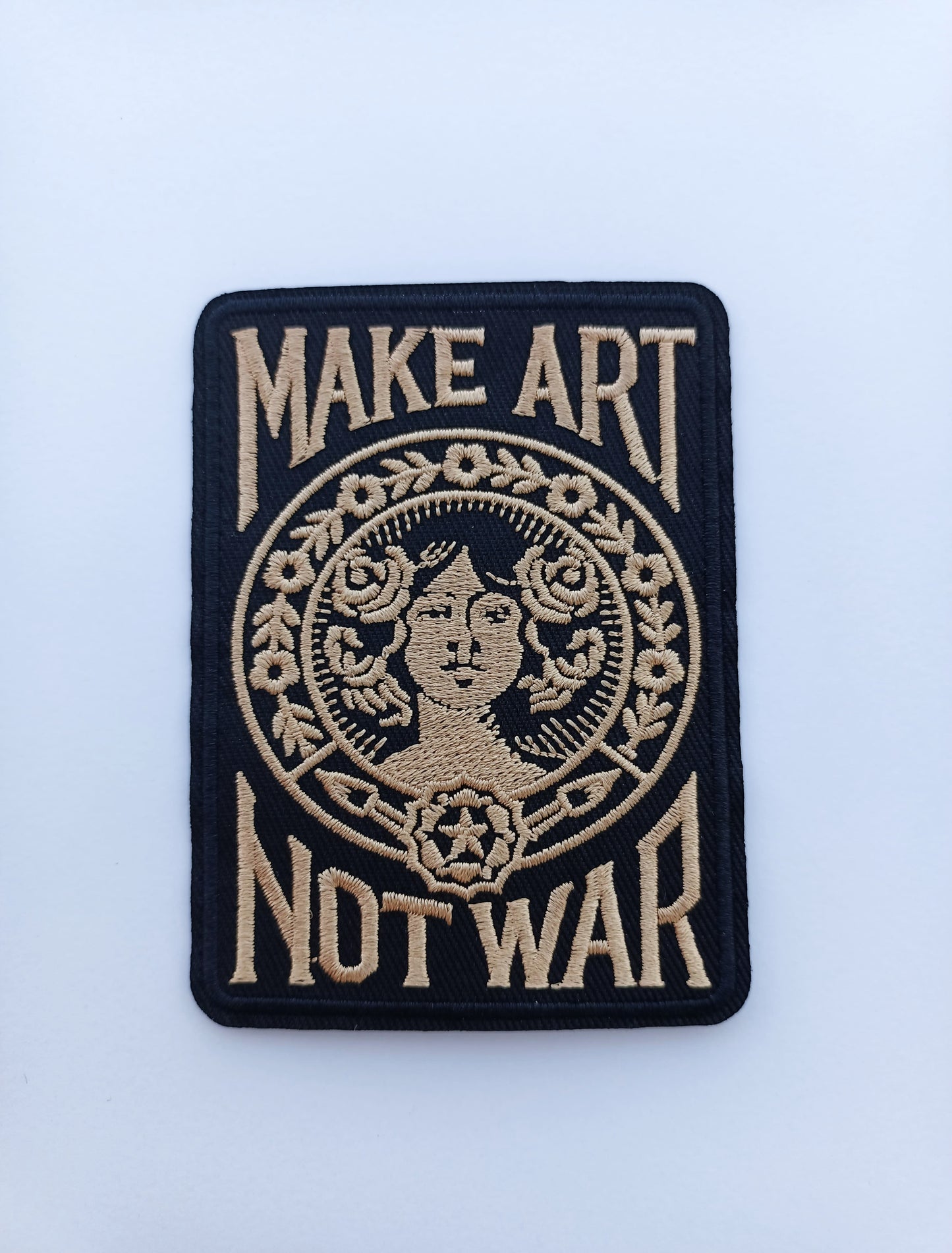 Parche rectangular negro y beige con la frase Make Art Not War y diseño gráfico clásico bordado.