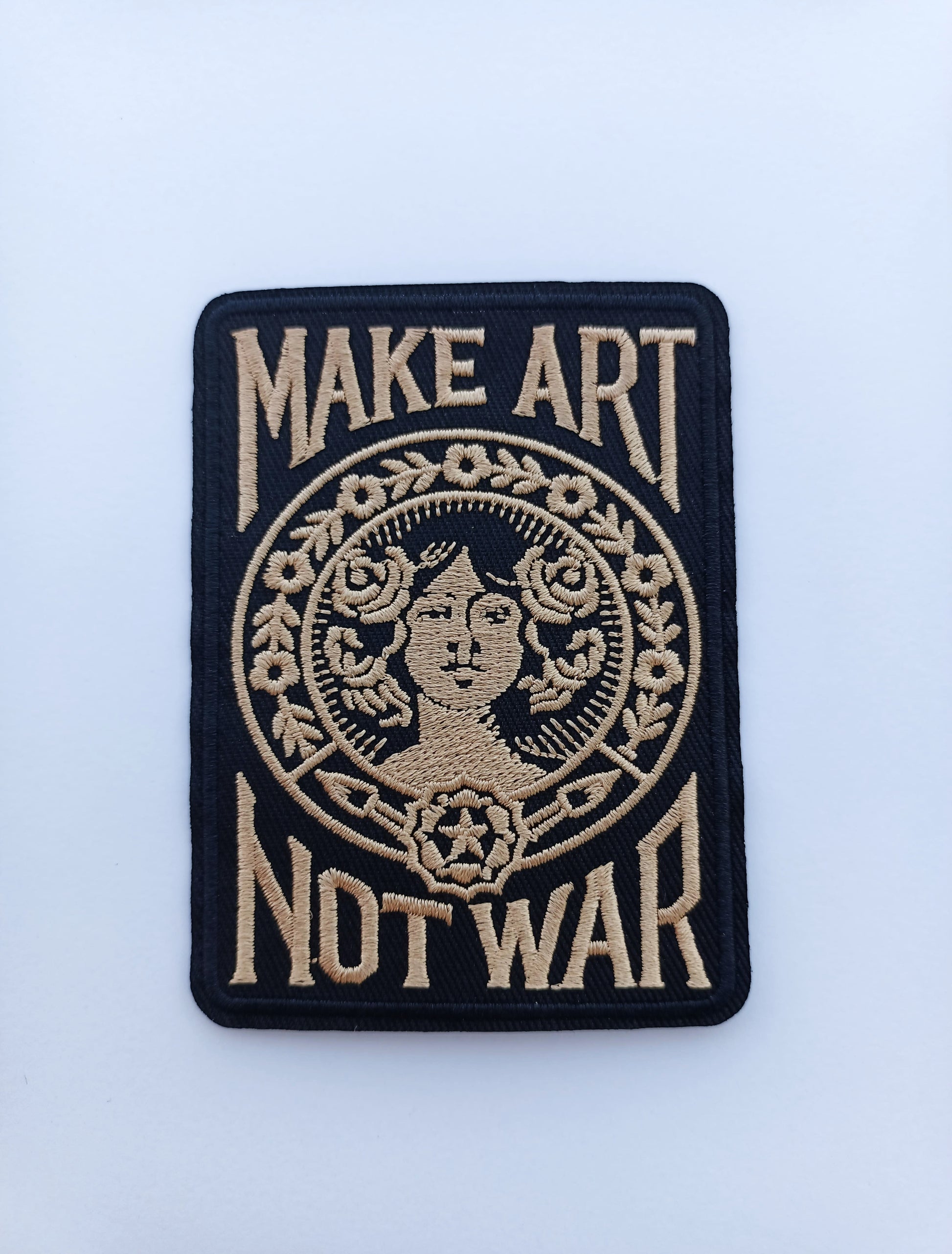 Parche rectangular negro y beige con la frase Make Art Not War y diseño gráfico clásico bordado.
