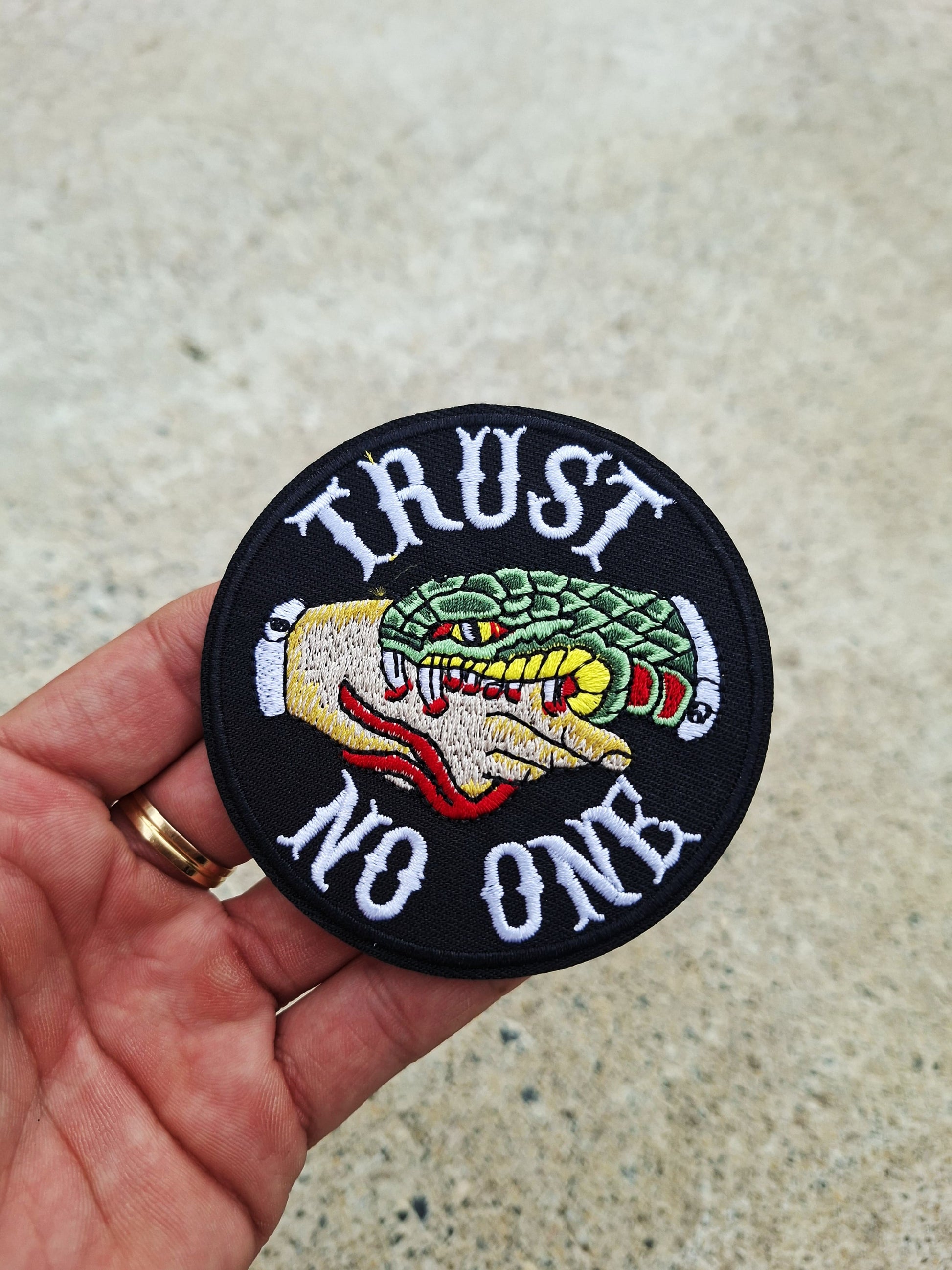 Parche bordado circular con mensaje rebelde Trust No One y motivos inspirados en tatuaje tradicional.