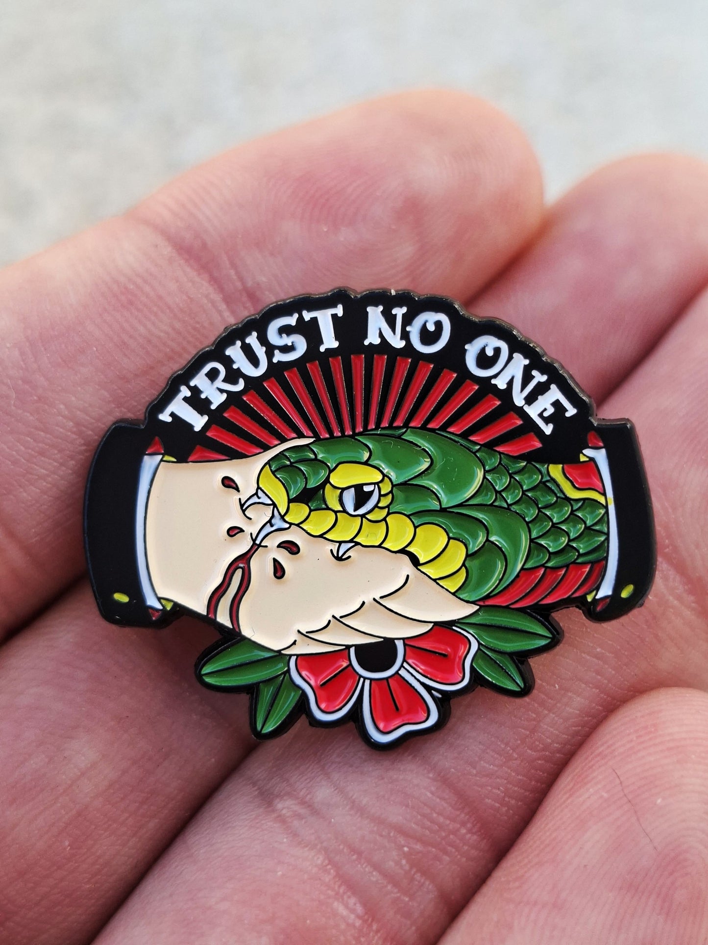 Pin metálico estilo old school americano con diseño de mano sujetando una serpiente y texto 'Trust No One'