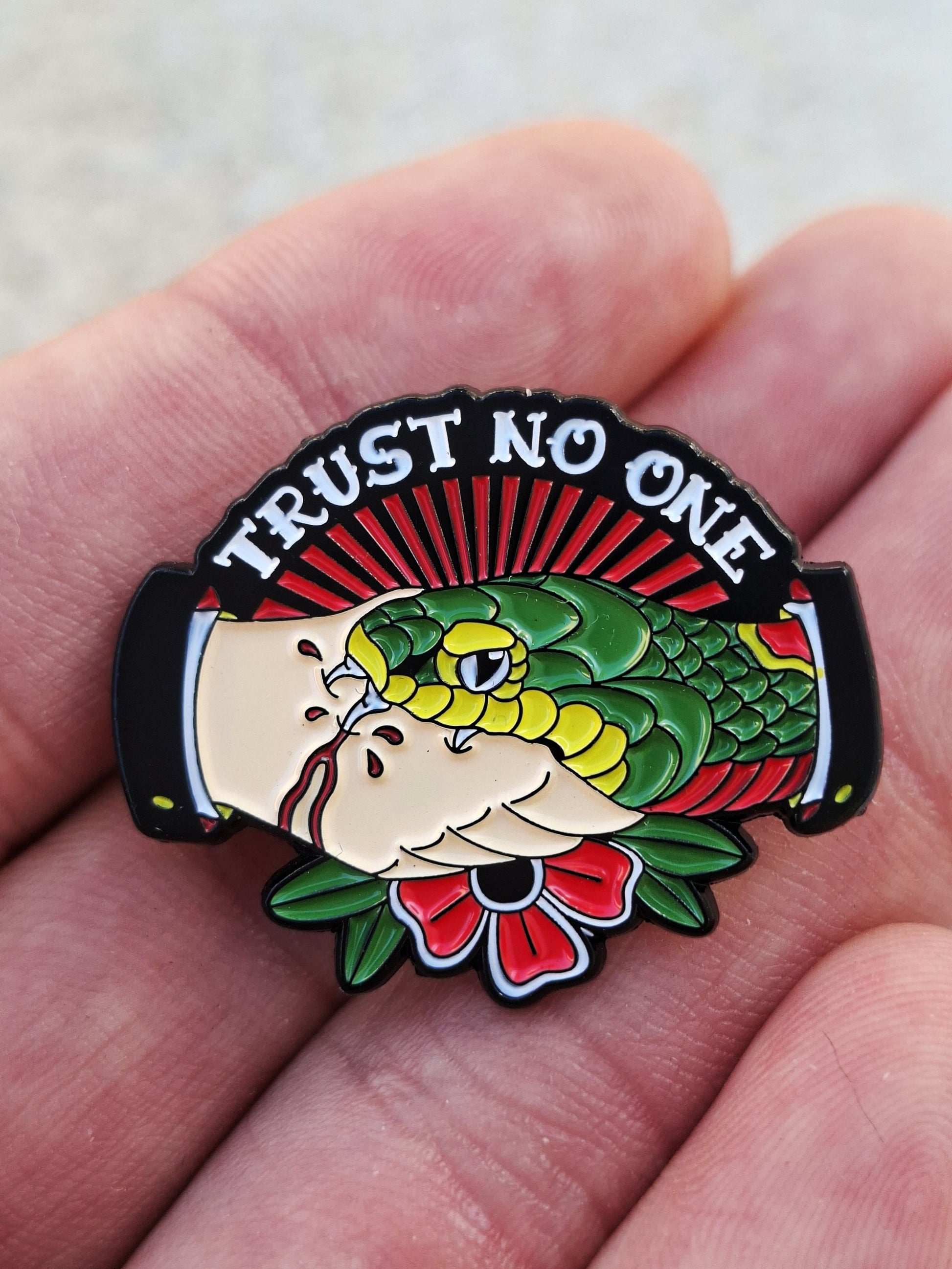 Pin metálico estilo old school americano con diseño de mano sujetando una serpiente y texto 'Trust No One'